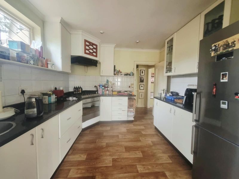 A functional kitchen featuring white cabinetry, dark granite countertops, a gas hob with extractor, and durable laminate flooring.