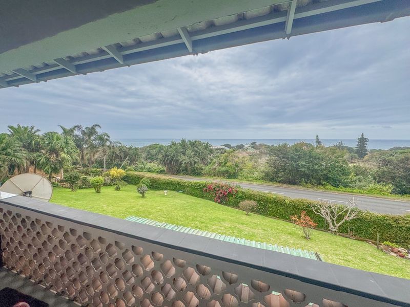 A balcony featuring a decorative breeze block balustrade, offering an elevated view over the garden, road, and distant ocean horizon.