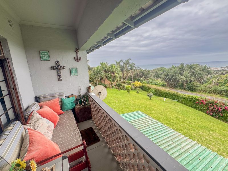 Covered balcony featuring a decorative breeze block balustrade, offering scenic views of the garden and distant coastline.
