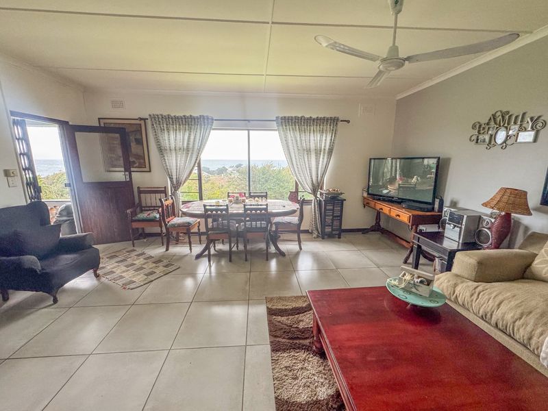 Spacious open-plan living and dining area featuring neutral tiled flooring, a ceiling fan, and large sliding doors with scenic views.