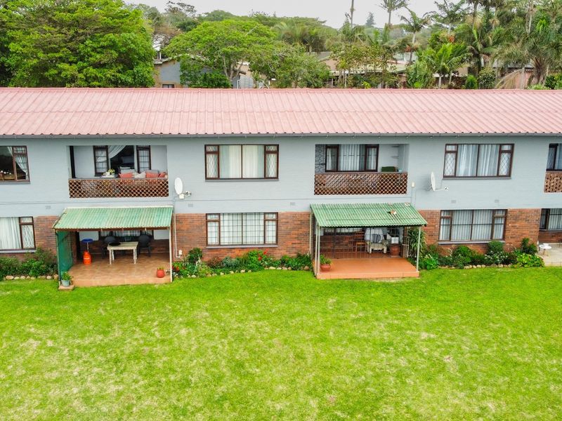 Aerial view of the rear elevation of a multi-story apartment building featuring ground floor patios, upper-level balconies, and a shared garden area.
