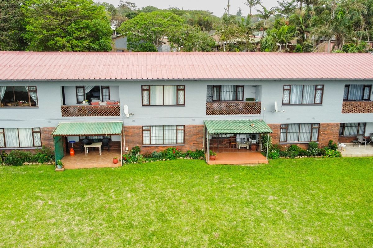 Aerial view of the rear elevation of a multi-story apartment building featuring ground floor patios, upper-level balconies, and a shared garden area.