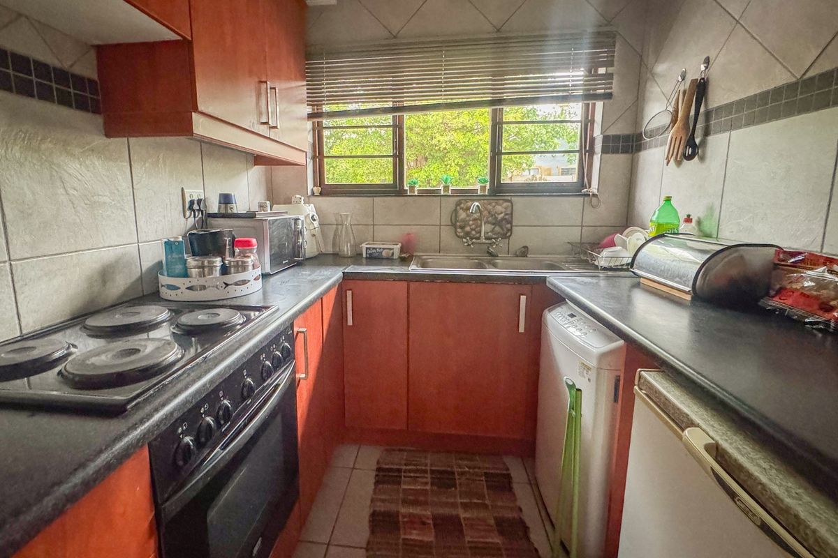 A compact kitchen featuring wooden cabinetry, dark laminate countertops, an integrated electric stove and oven, and a double basin sink with tiled backsplash.