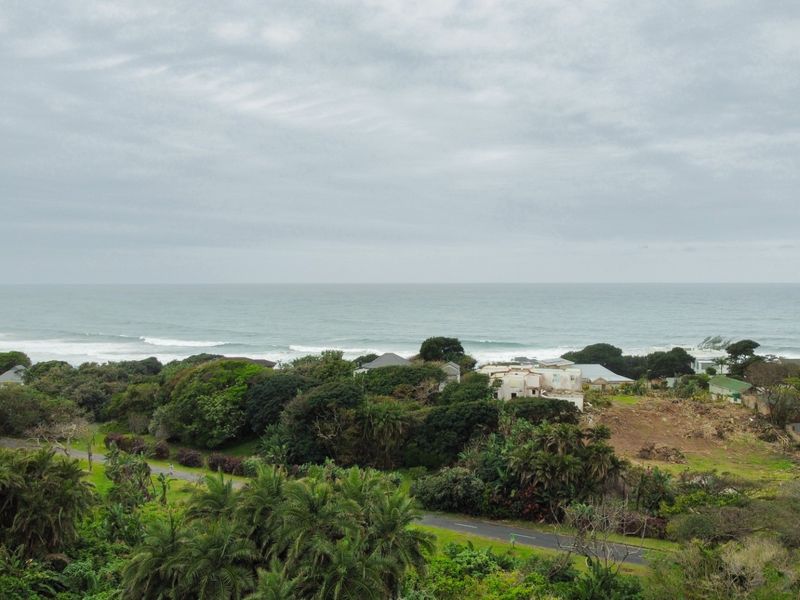 An elevated aerial view showcasing the coastal landscape, surrounding greenery, and nearby residential properties with a clear view of the ocean.