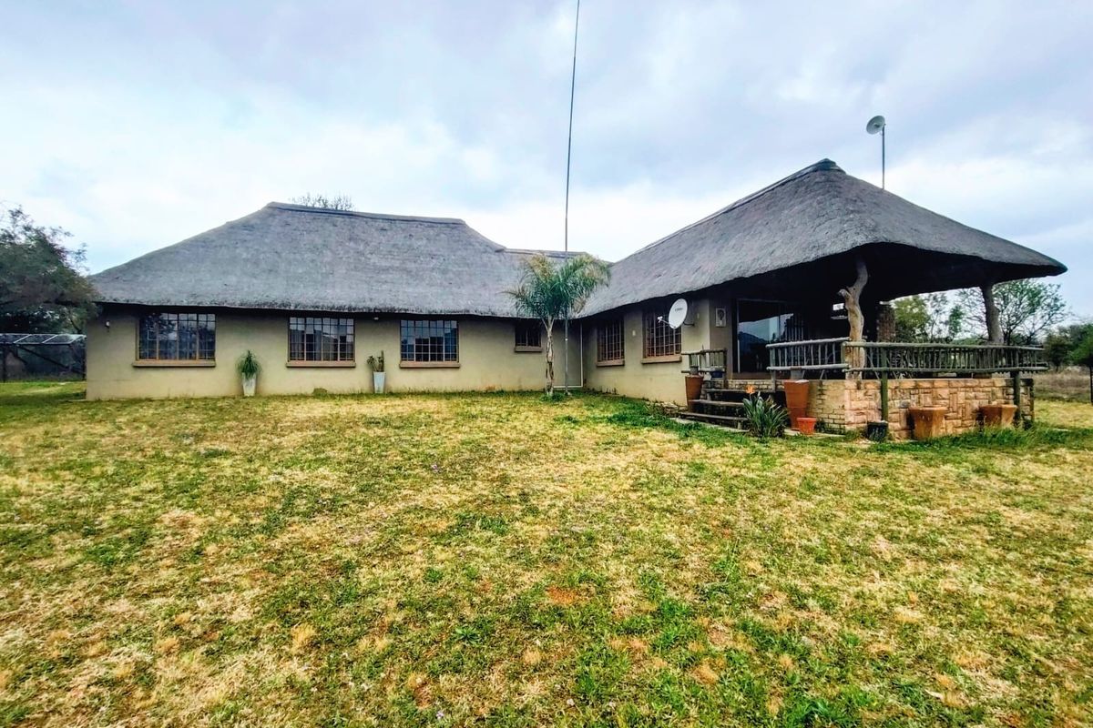 Rear view of a small holding property featuring a traditional thatched roof, a covered patio with stone base, and expansive surrounding grounds.