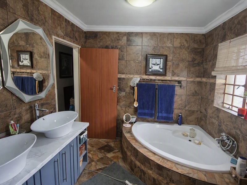 A bathroom featuring a double vanity with vessel sinks, a corner bathtub, and full-height wall tiling.