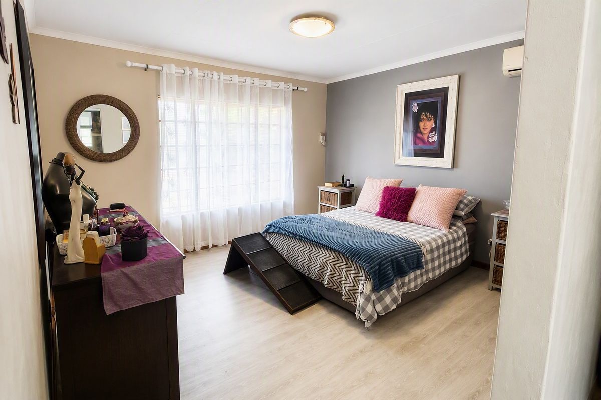 A well-maintained bedroom featuring light laminate flooring, a neutral color palette, and a wall-mounted air conditioning unit.