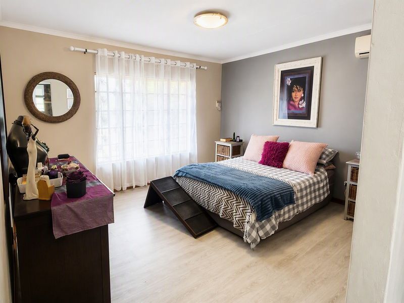 A well-maintained bedroom featuring light laminate flooring, a neutral color palette, and a wall-mounted air conditioning unit.
