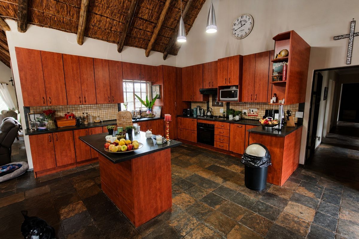 Spacious kitchen featuring a high thatched ceiling with exposed rafters, dark wood cabinetry, a central island, and durable stone flooring.