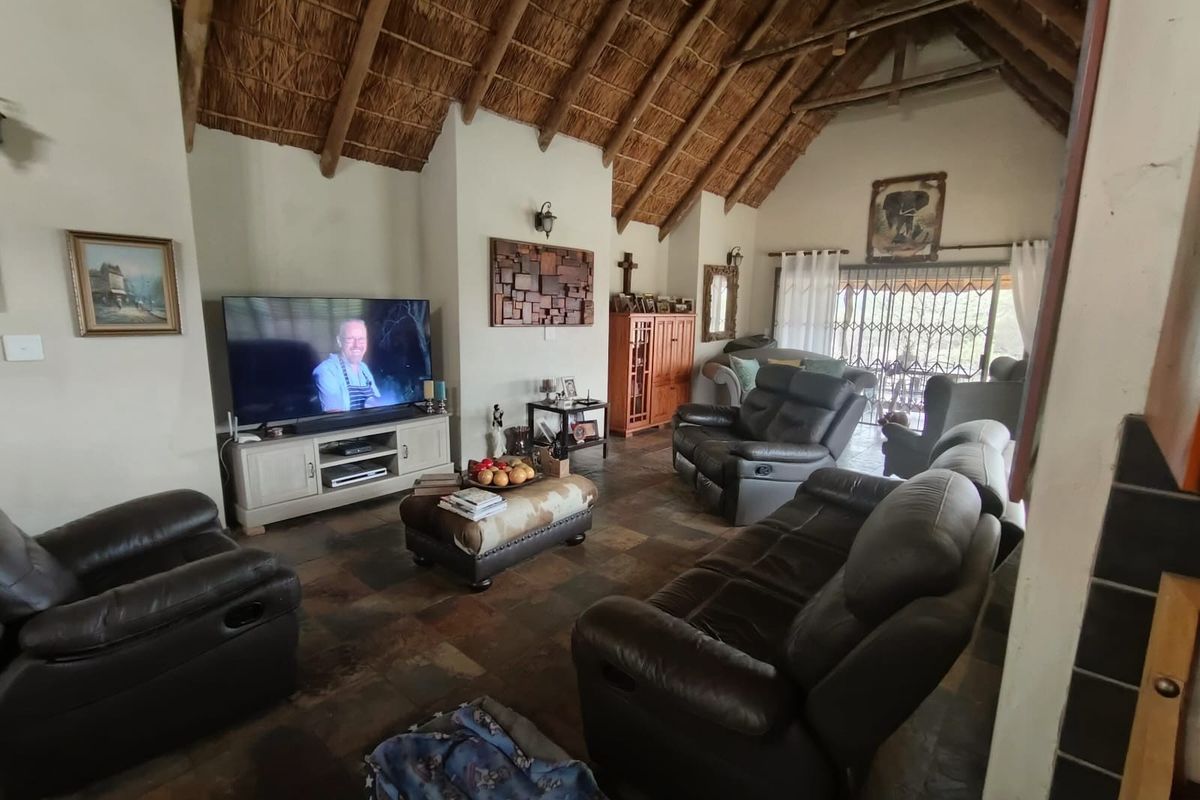 Spacious living room featuring a high vaulted thatched ceiling with exposed timber trusses and durable slate tile flooring, leading to an outdoor patio area.