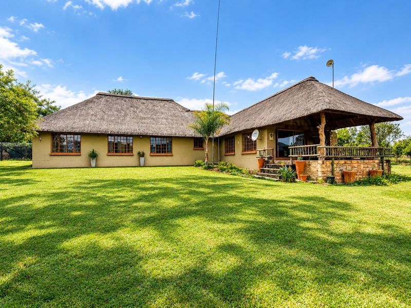 Rear view of a small holding property featuring a traditional thatch roof, stone-clad patio area, and expansive green lawn.