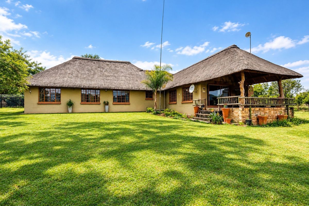 Rear view of a small holding property featuring a traditional thatch roof, stone-clad patio area, and expansive green lawn.