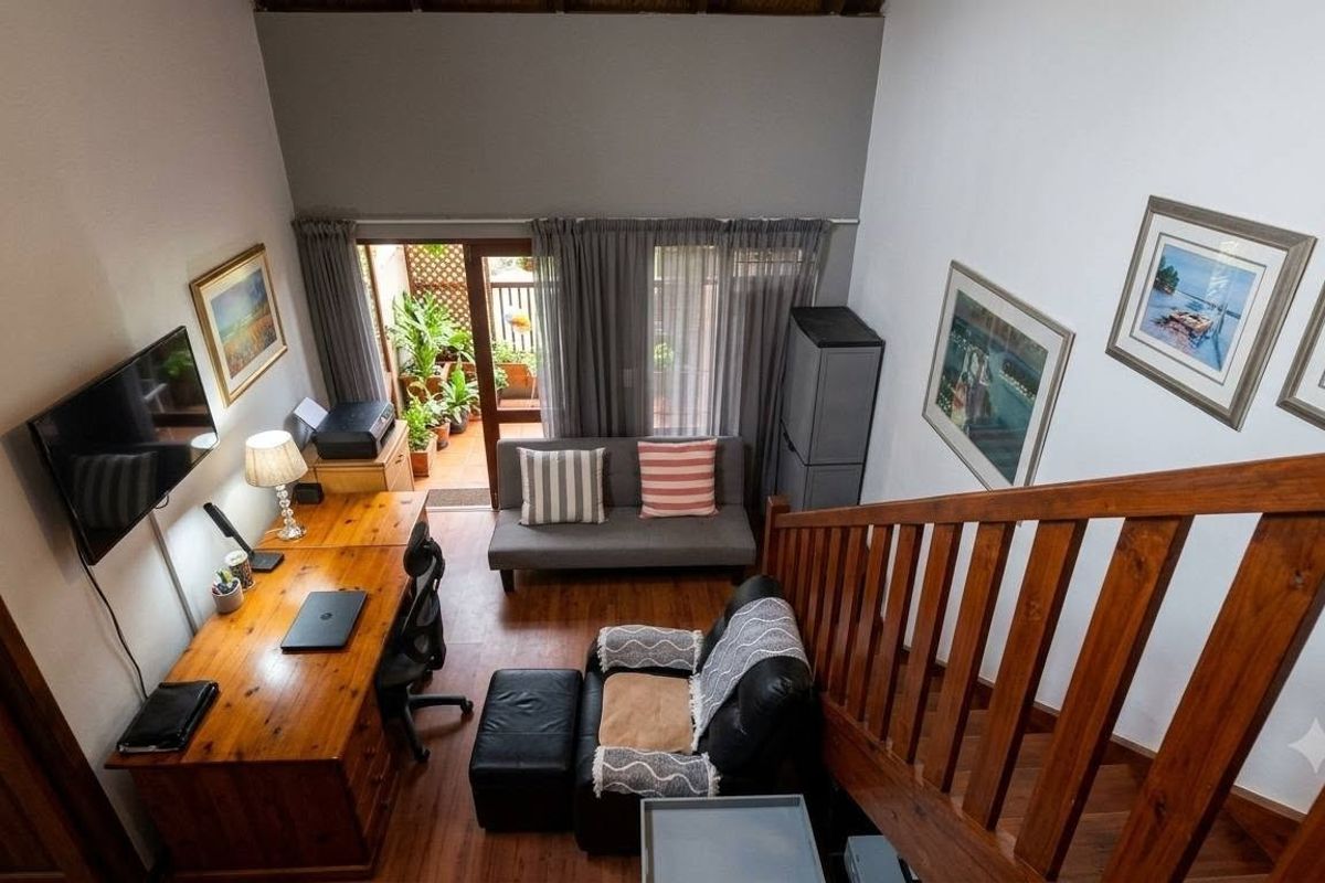 A bright living area featuring high vaulted ceilings, laminate flooring, and a wooden staircase leading to an upper level, with access to a patio.
