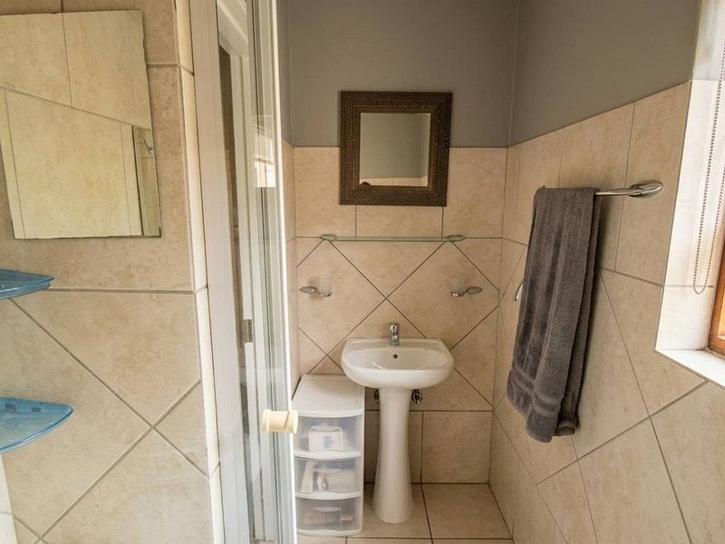 A functional bathroom featuring a pedestal basin, shower enclosure, and neutral ceramic wall and floor tiling.