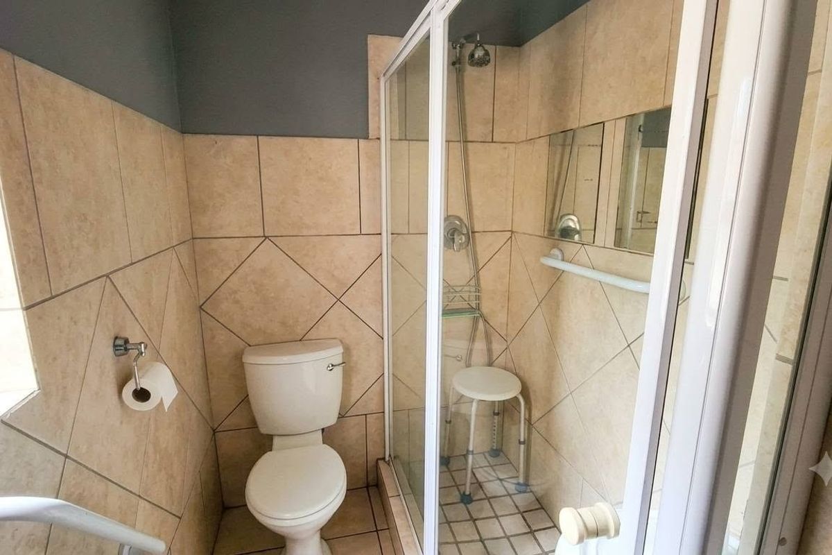 A functional bathroom featuring a shower enclosure, toilet, and tiled walls with a safety grab rail installed.