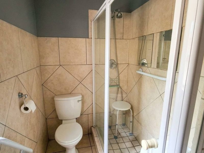 A functional bathroom featuring a shower enclosure, toilet, and tiled walls with a safety grab rail installed.