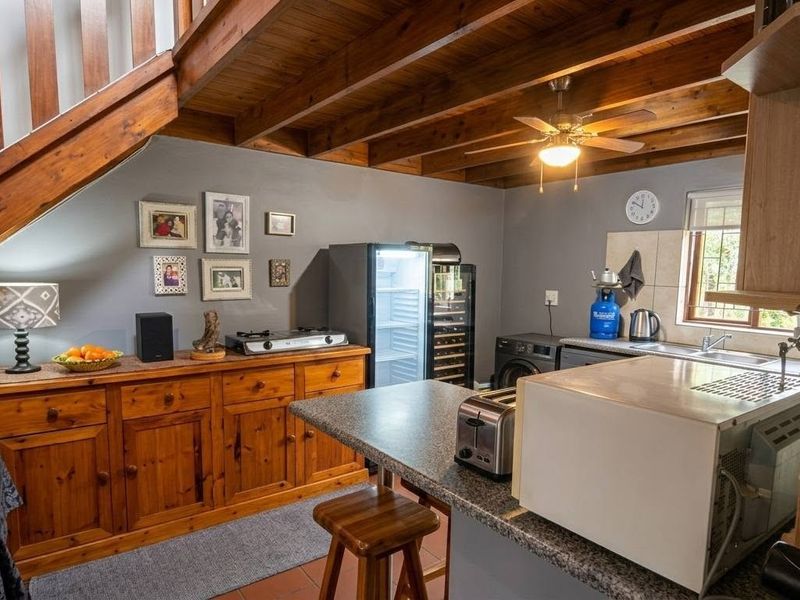 A rustic kitchen featuring exposed timber ceiling beams, a wooden staircase, granite countertops, and a functional layout with integrated sink and cabinetry.