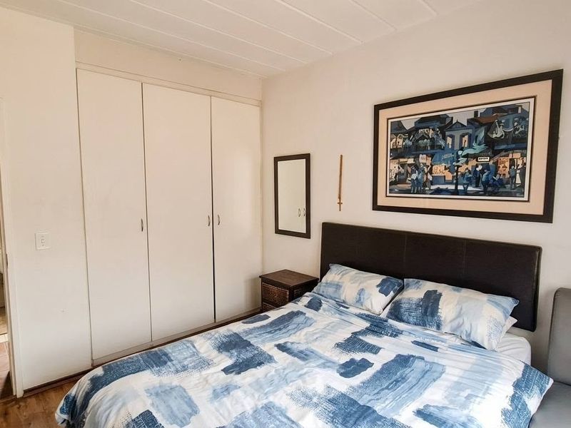 A bedroom featuring built-in cupboards and laminate flooring, with an adjacent view into a tiled bathroom area.