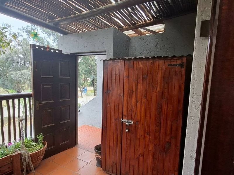 A covered balcony area featuring tiled flooring, a wooden balustrade, and a rustic thatched roof structure.