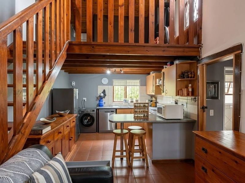 Open-plan living area featuring a wooden staircase leading to a mezzanine level, combined with a functional kitchen space with tiled flooring.