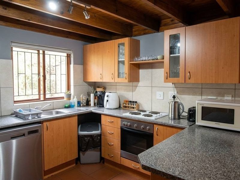 A functional kitchen featuring laminate cabinetry, granite countertops, a built-in oven with electric hob, and distinctive exposed timber ceiling beams.