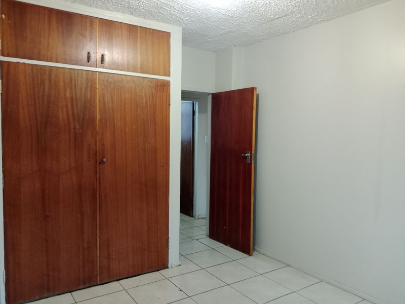 An empty bedroom featuring built-in wooden cupboards, tiled flooring, and a textured ceiling, offering a blank canvas for personalization.