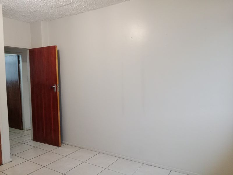 An empty bedroom featuring tiled flooring, a solid timber door, and a textured ceiling, providing a blank canvas for interior design.