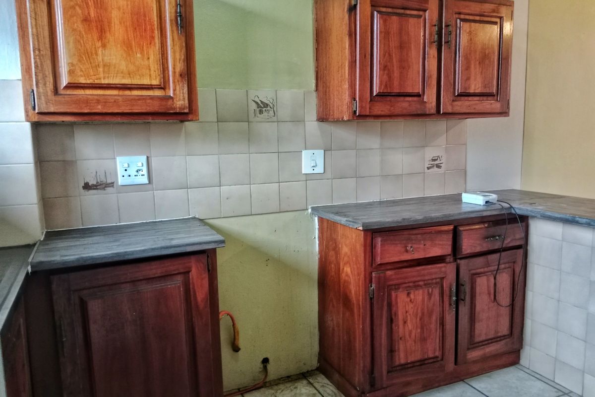 A dated kitchen featuring wooden cabinetry, laminate countertops, and tiled backsplash, currently vacant and requiring cosmetic updates to modernize the space.