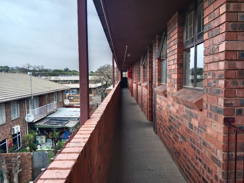 An exterior open-air walkway featuring exposed brick walls and tiled flooring, providing access to apartment units.