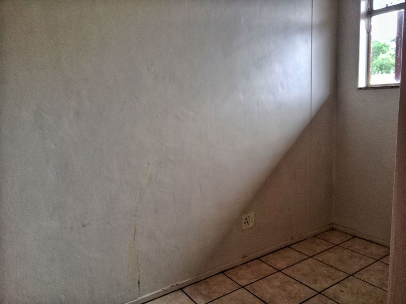 An empty bedroom featuring tiled flooring and a single window, currently showing signs of wall staining and surface wear.