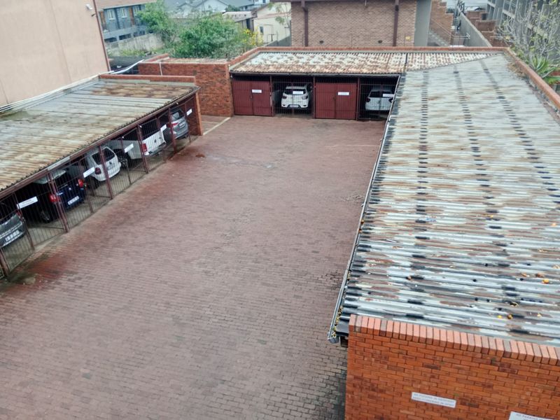 An elevated view of a communal parking area featuring multiple covered garage bays with metal gates and brick paving.