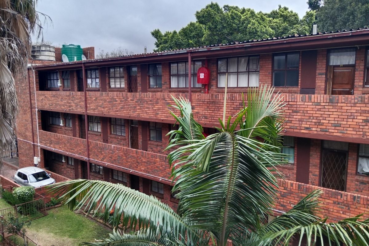 Exterior view of a multi-story apartment building featuring face brick construction, metal roofing, and communal access walkways.