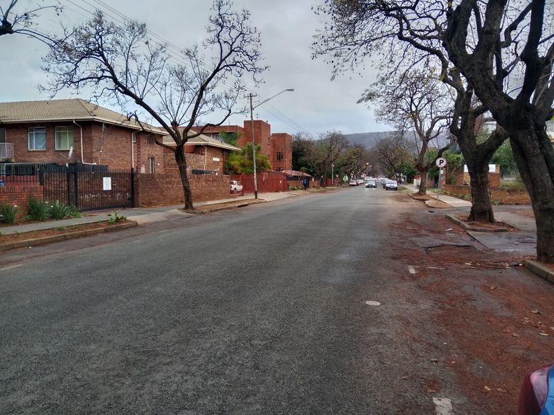 A view of the residential street showing the surrounding neighbourhood, asphalt road, and brick boundary walls of the apartment complex.