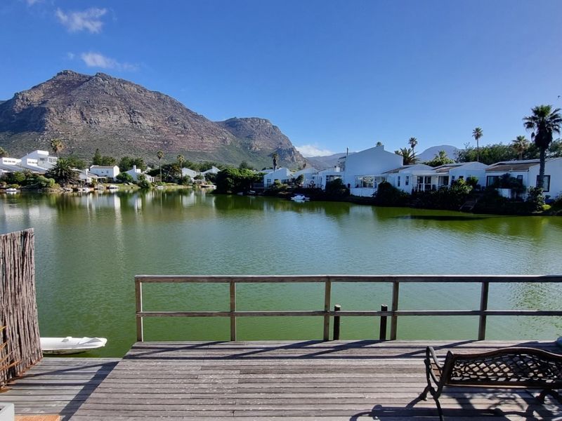A scenic view overlooking a tranquil lagoon with surrounding residential properties and mountain vistas, featuring a private timber deck.