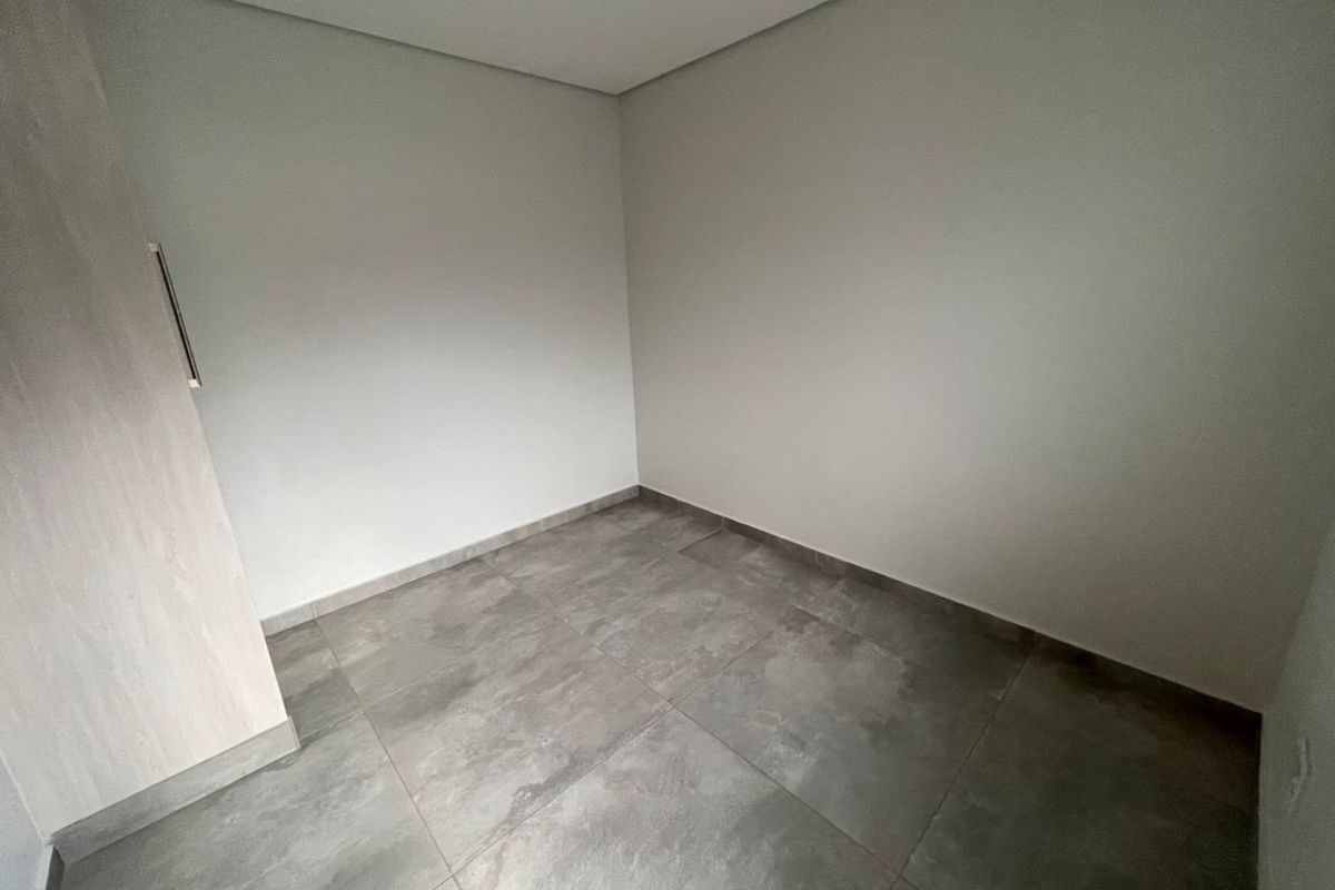 A clean, empty bedroom featuring neutral wall finishes, large format grey floor tiles, and a built-in cupboard with a modern finish.