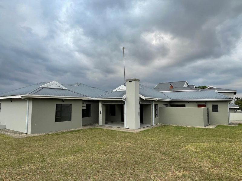 Rear view of a modern house featuring a covered patio, corrugated metal roofing, and a spacious lawn area.