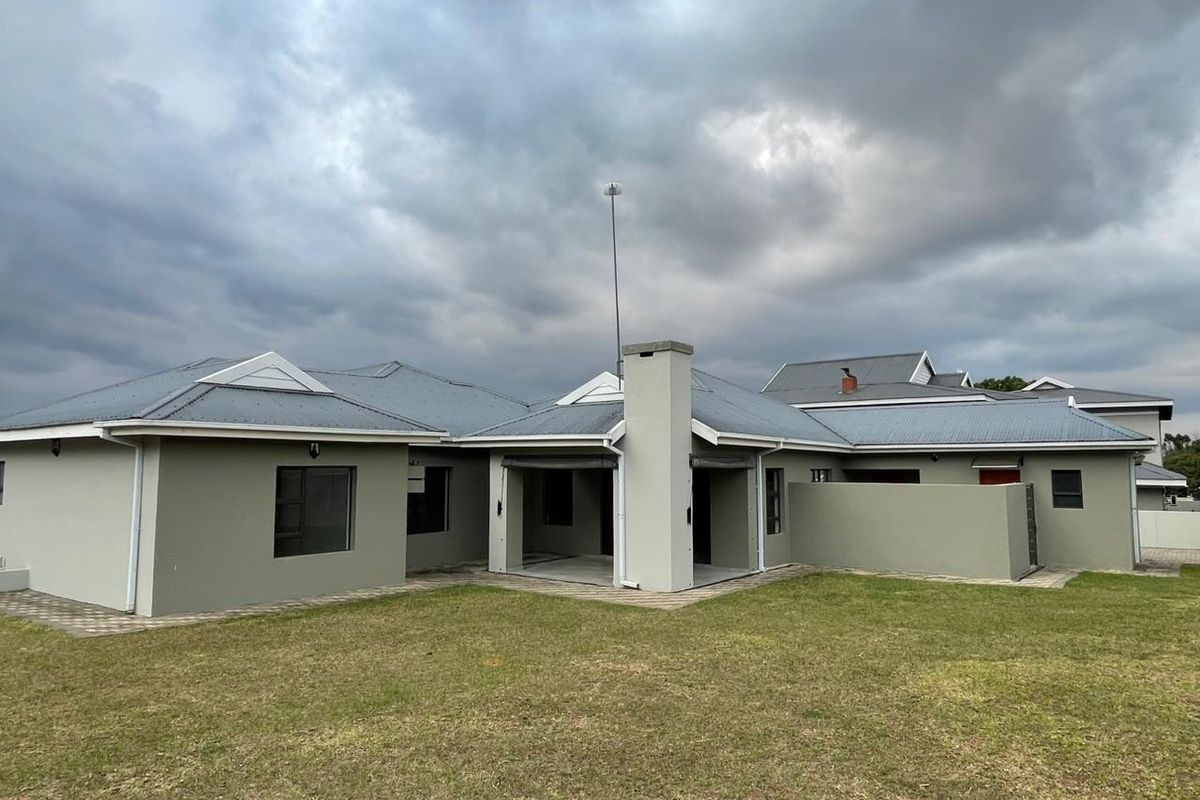Rear view of a modern house featuring a covered patio, corrugated metal roofing, and a spacious lawn area.