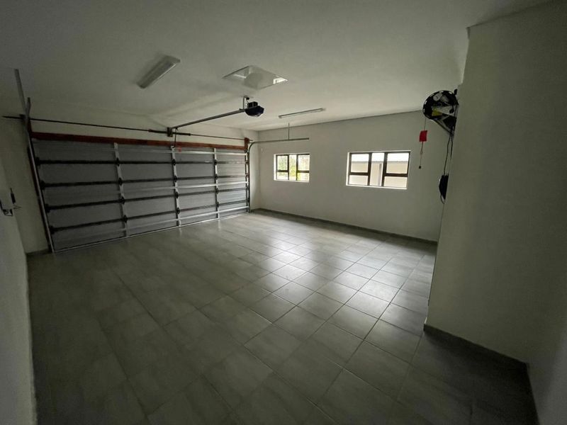 A spacious, clean, and well-maintained double garage featuring tiled flooring, a sectional door, and ample natural light through aluminium windows.