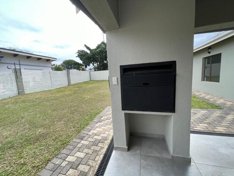 Covered patio area featuring a built-in braai, tiled flooring, and direct access to the paved walkway and garden.