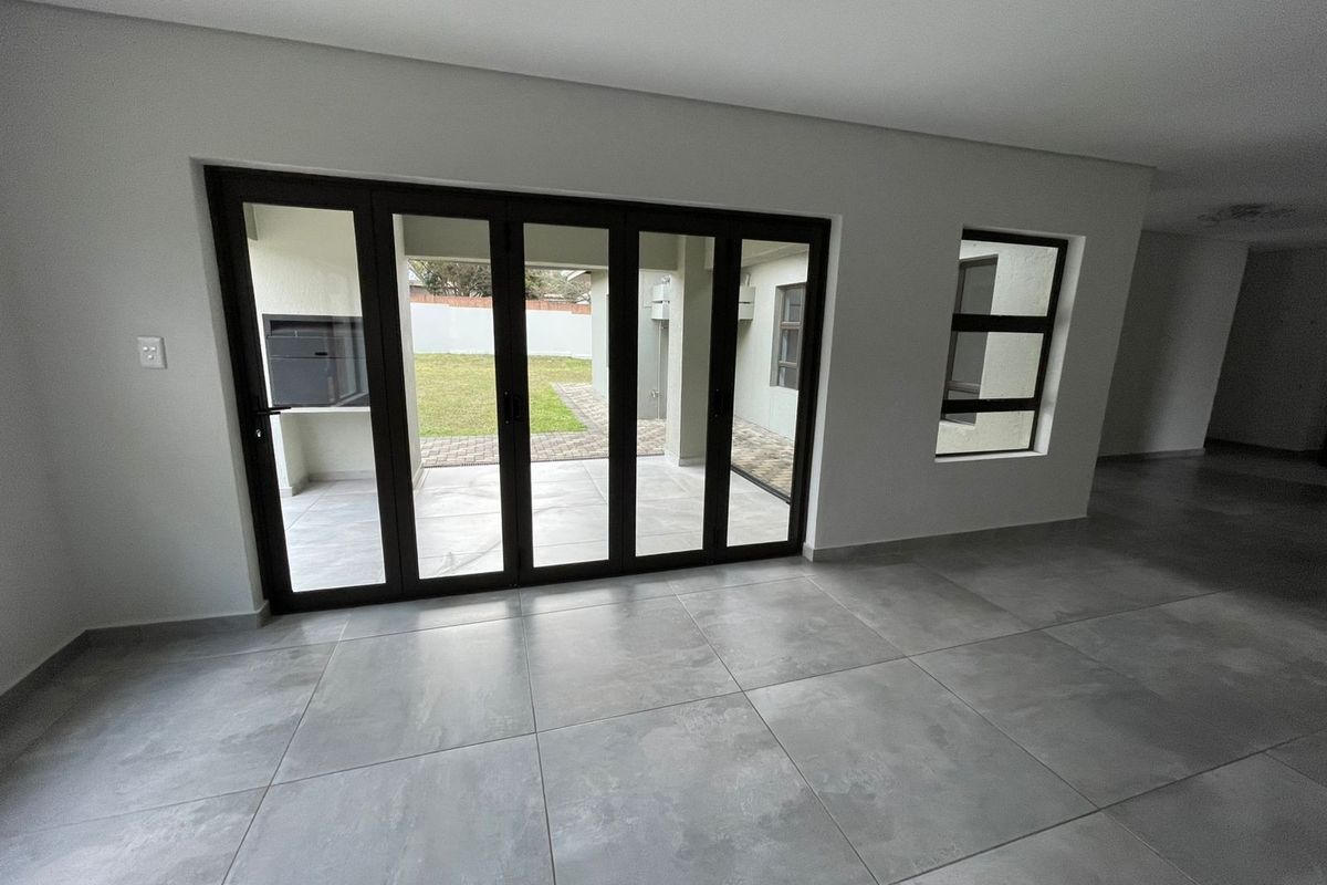 Spacious living area featuring large format floor tiles and modern black aluminium stacker doors opening onto a patio with a built-in braai.