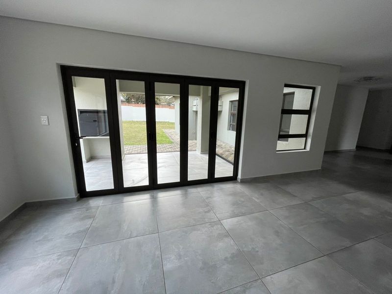 Spacious living area featuring large format floor tiles and modern black aluminium stacker doors opening onto a patio with a built-in braai.