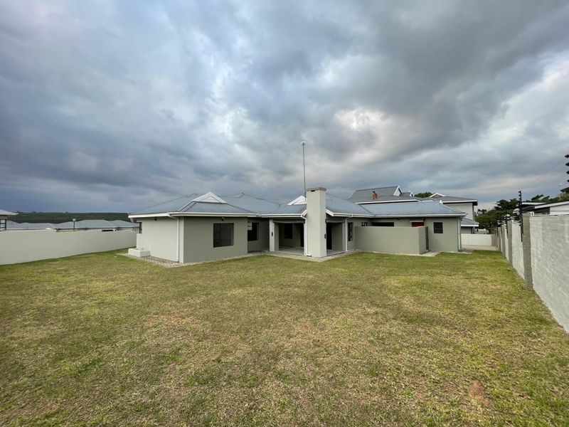 Rear view of the property featuring a spacious lawn, covered patio area, and well-maintained masonry boundary walls under a metal roof structure.