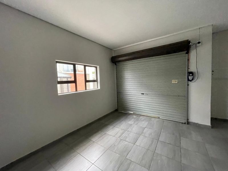 A clean, empty garage space featuring tiled flooring, a secure roller shutter door, and a side window providing natural light.