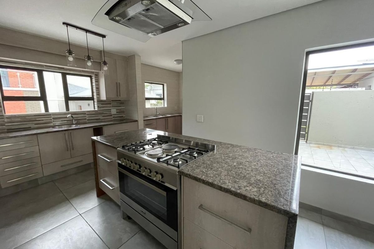 Modern kitchen featuring granite countertops, built-in cabinetry, a gas stove with extractor fan, and tiled flooring, offering a clean and functional workspace.