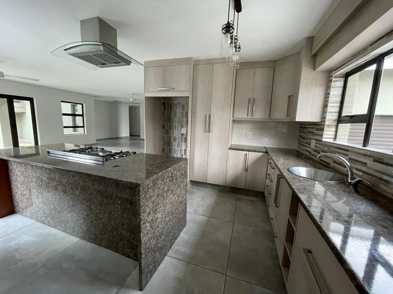 Modern open-plan kitchen featuring granite countertops, built-in cabinetry, a central island with a gas hob, and tiled flooring throughout the living space.