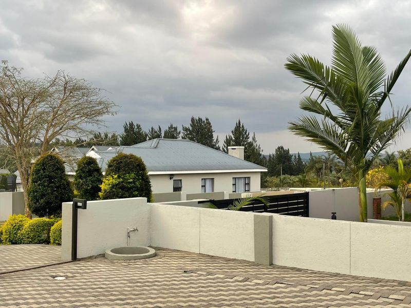 A view of the property exterior featuring a paved driveway, boundary wall, and metal gate with a view of the main house structure.