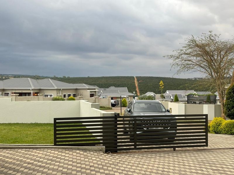 Front view of the property featuring a paved driveway, modern slatted metal gate, and perimeter boundary wall with electric fencing.