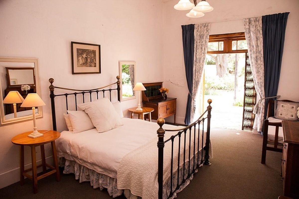 A bedroom featuring carpeted flooring, a ceiling light fixture, and a timber door frame leading to an outdoor area, with visible wall plaster cracks.