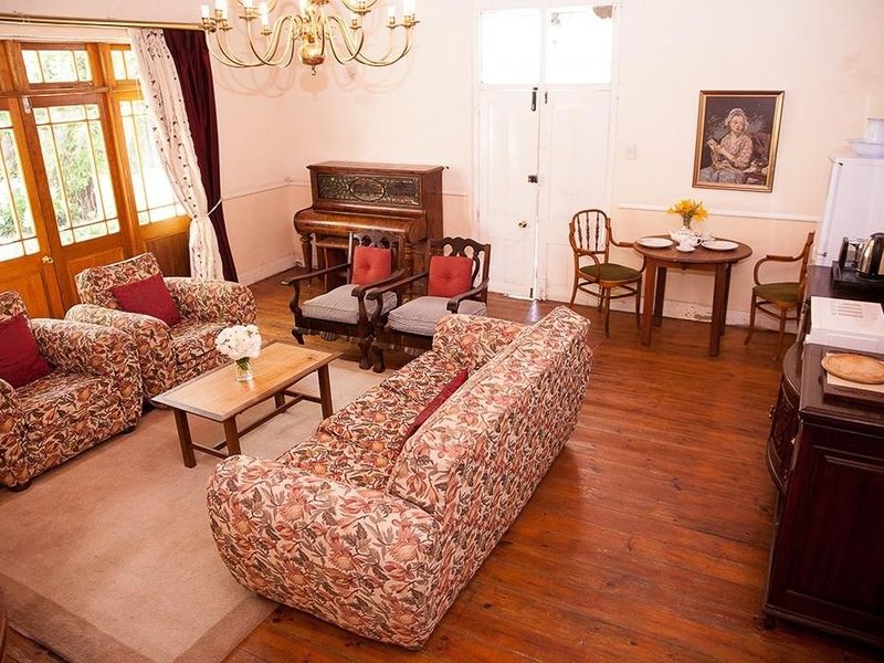 A spacious living room featuring original hardwood flooring, a classic chandelier, and timber-framed glass doors leading to the exterior.