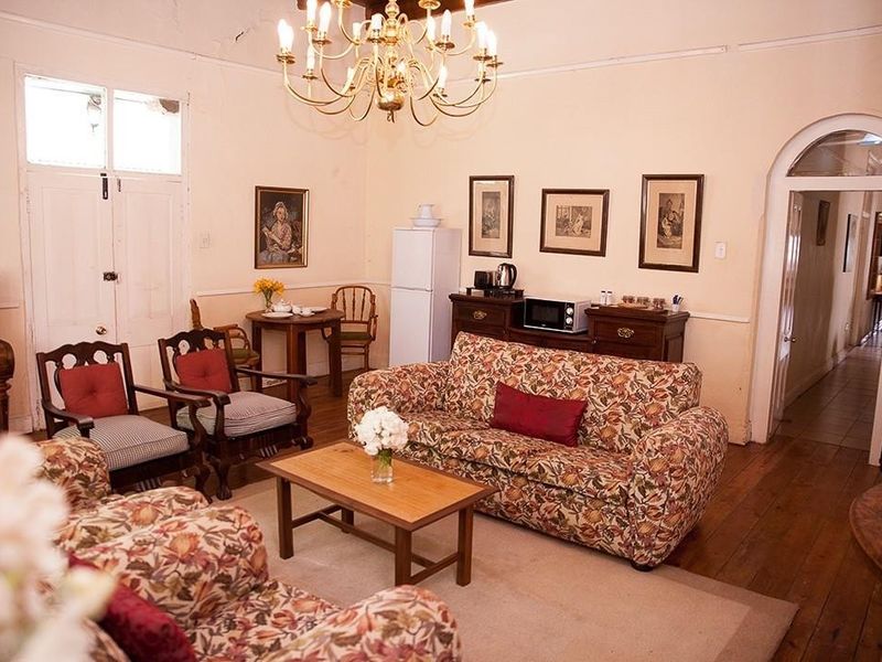 A traditional living room featuring hardwood flooring, an arched doorway, and a classic chandelier, with visible ceiling plaster cracks requiring maintenance.